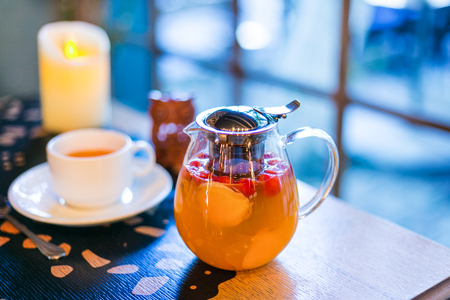 Delicious tea with ginger, apple and and rosehip in a transparent teapot. Cup and candle in the background out of focusの写真素材
