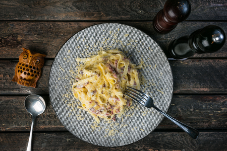 Pasta Carbonara with bacon and parmesan, served with the cutlery and pepper mill on the wooden background.の写真素材