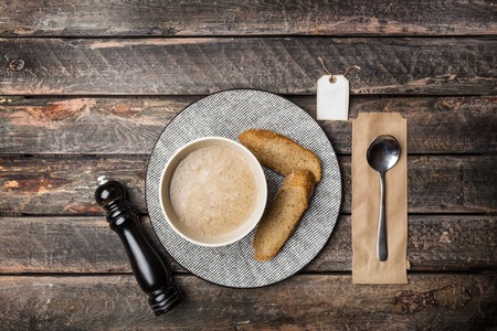 Mushroom cream soup with croutons served in the ceramic bowl and spoon, decorated with the pepper mill and sticker for your logo or text.の写真素材