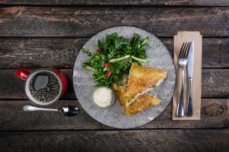 Strudel with chicken, zucchini and vegetable salad, served on the ceramic plate with the cutlery and the cup of coffee.の写真素材