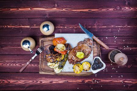 Delicious grilled steak with assorted roast vegetables and corn. There is a pepper grinder, sauce...