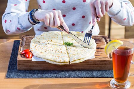hychiny, tortilla dough with cheese and potatoes, on cutting board. With female hands and a cup of...