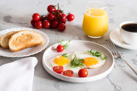 fried eggs with tomatoes and herbs, toast, coffee and juiceの写真素材