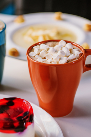 Hot chocolate with marshmallows hold in hand. Cocoa. On white table in a restaurantの写真素材