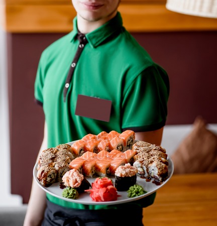 The guy is holding a round tray with sushi and rolls. close-up, big sushi setの写真素材