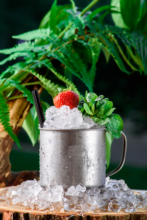 Beautiful cocktail in a pannikin with ice and strawberries on the background of green leaves. space. close up.の写真素材