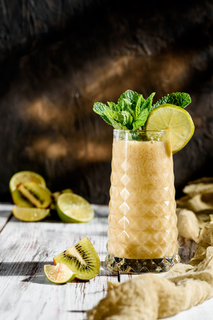delicious smoothies from apineapple and kiwi fruit in a beautiful glass decorated with mint on a light wooden background. on fruit background. space. close-upの写真素材