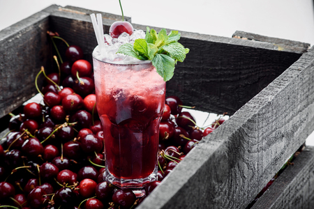 Red cocktail with ice, mint and cherry on a berry background. cherry box. close-up. spaceの写真素材
