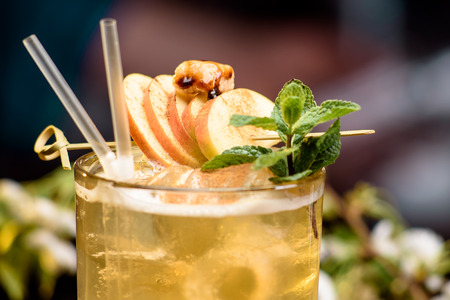 yellow summer cocktail decorated with apple slices and mint on a wooden table on a floral background close up. detailsの写真素材