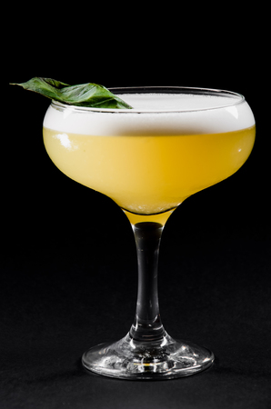 Beautiful yellow cocktail with white froth decorated with mint in a glass chalet isolated against a blackの写真素材