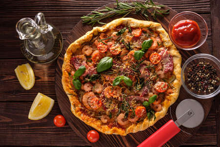 Pizza with shrimps, tomatoes, cheese and herbs on a wooden background