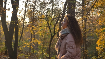 Portrait in profile of gorgeous curly-haired caucasian girl walking in autumnal park and observing...