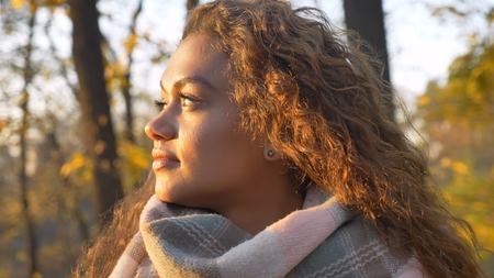 Portrait in profile of pretty curly-haired caucasian girl watching calmly leftwards in autumnal...