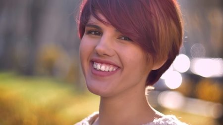 Close-up portrait of young cool caucasian pink-haired girl watching happily into camera on sunny...