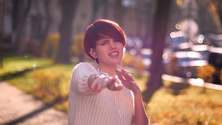 Young caucasian pink-haired girl with earphones listening to music and dancing actively on sunny...