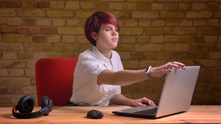 Closeup shoot of young attractive hipster female video blogger with dyed hair fixing the laptop and streaming live with headphones on the tableの写真素材
