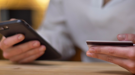 Close-up portrait of young businesswoman doing transactions using credit card and smartphone on office background.の写真素材