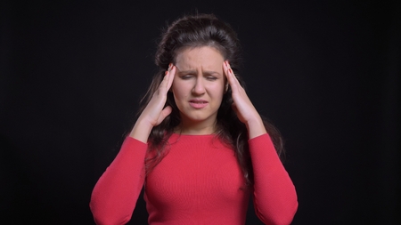 Closeup portrait of attractive middle-aged caucasian female having a headache in front of the camera with background isolated on blackの写真素材