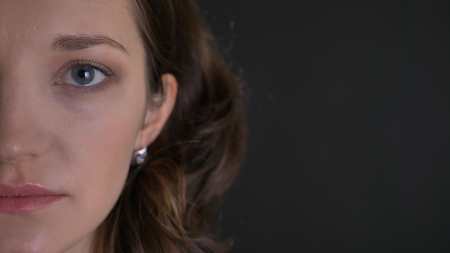 Half-portrait of cute young brunette woman watching into camera modestly on black background.の写真素材