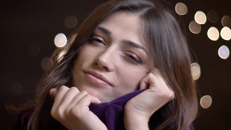 Close-up portrait of beautiful caucasian brunette girl watching gladly into camera and hiding in her...