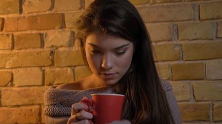Closeup shoot of young attractive caucasian female holding a cup of warm tea being joyful and...