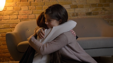 Closeup portrait of two young pretty caucasian girls hugging with love indoors in a cozy apartmentの写真素材