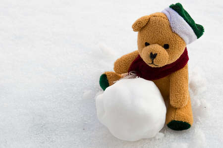 Cute teddy bear sits in the snow with a snowballの写真素材