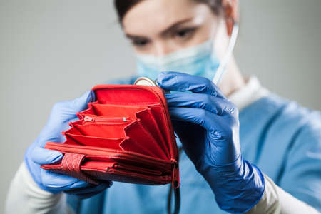 Coronavirus COVID-19 corona virus disease global pandemic crisis causing world financial recession crash,female caucasian doctor examining an empty red wallet with stethoscope,economy recovery conceptの写真素材