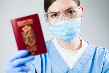 Doctor or nurse at airport customs security check holding a passport, no entry quarantine and isolation order ban, COVID-19 virus disease epidemic, viral Coronavirus global worldwide pandemic outbreakの写真素材