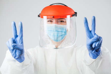 Coronavirus COVID-19 global pandemic crisis,female medic in protective suit gesturing victory,raised...