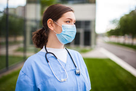 Serious female caucasian doctor looking away with worried facial expression,lost hope due to high mortality rate death toll,Coronavirus COVID-19 pandemic crisis,overworked exhausted EMS staff portraitの写真素材