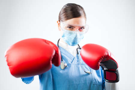 Young female caucasian doctor wearing blue uniform and red boxing gloves, professional and confident, fighting off a disease, immunity and immune system antibodies overcoming viral antigens conceptの写真素材