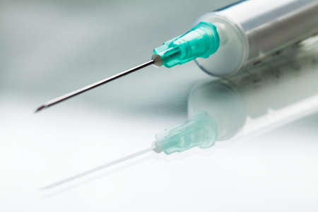Injection shot, needle & syringe jab on reflective surface,COVID-19 Coronavirus pandemic search for potential vaccine cure,vaccination concept illustrationの写真素材