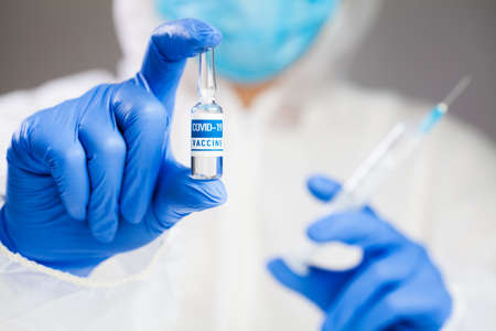 Medical laboratory scientist technician holding a syringe and COVID-19 coronavirus disease vaccine...