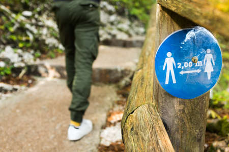 Blue round sign on a wooden fence by a park trail informing people to keep 2 meter 6 feet physical social distance from each other,prevent & protect Coronavirus COVID-19 virus disease infection spreadの写真素材