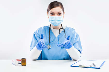 Young female UK NHS doctor wearing protective glove and face mask,talking online to patient,young GP...