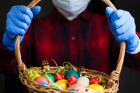 Person holding Easter basket wearing blue protective gloves and face mask, 2021 holiday celebration...
