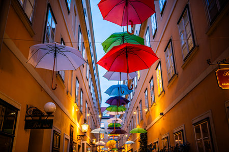 Colorful umbrellas decorating a narrow street, between old European yellow buildings. Colored...