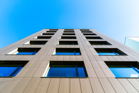 Vertical Perspective of a Modern Building with Reflective Windows Against a Clear Blue Skyの写真素材