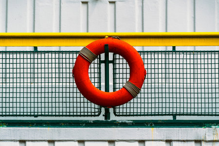 Bright Red Lifebuoy Mounted on a Colorful Rail with Industrial Backdropの写真素材
