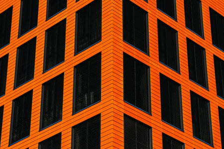 Modern office facade with orange cladding and dark blinds forming a repetitive geometric grid
