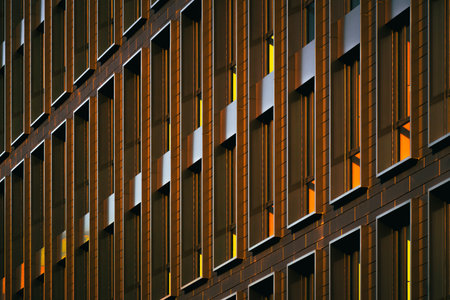 Modern building faÃ§ade with repeating vertical windows lit by warm sunlight, creating strong...