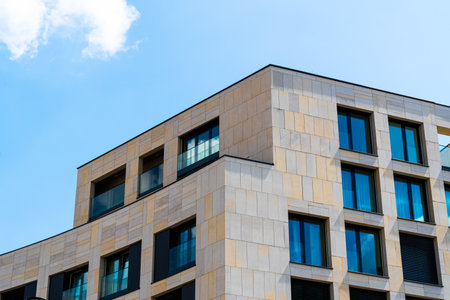Modern residential corner building with beige stone cladding and blue windowsの写真素材