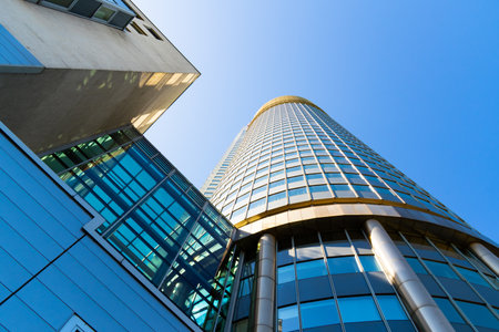 Modern curved office tower with glass grid facade rising against a vivid blue clear sky background