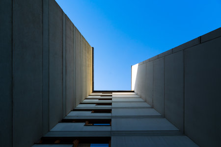 Minimalist architectural perspective of modern concrete building walls converging toward a bright blue skyの写真素材