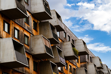 Modern wooden residential building with angular concrete balconies and geometric design against...