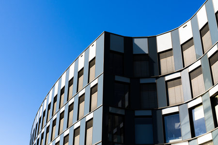 Contemporary office building with metallic facade and geometric glass design under clear deep blue...