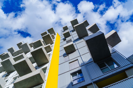 Contemporary residential building with projecting concrete balconies and yellow accent under bright...