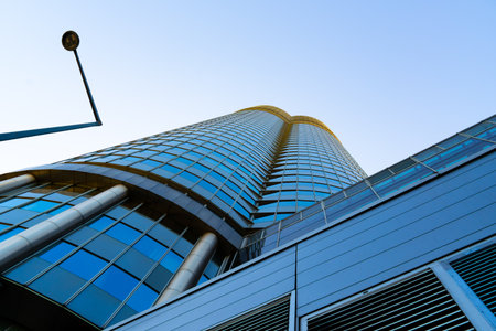Modern curved office tower with glass grid facade rising against a vivid blue clear sky background