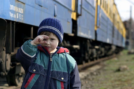 little boy in hat and jacket playing by a railwayの写真素材